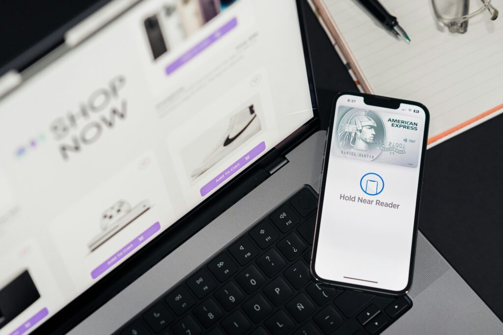 pexels-photo-29502378-29502378 Smartphone with payment terminal app next to laptop displaying online shopping site.