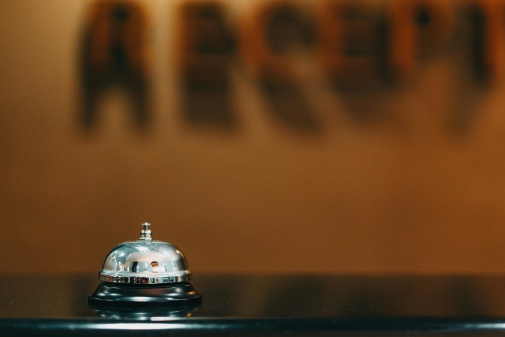 pexels-photo-7821343-7821343 Close-up image of a silver hotel bell on a black surface with 'RECEPTION' blurred in the background.